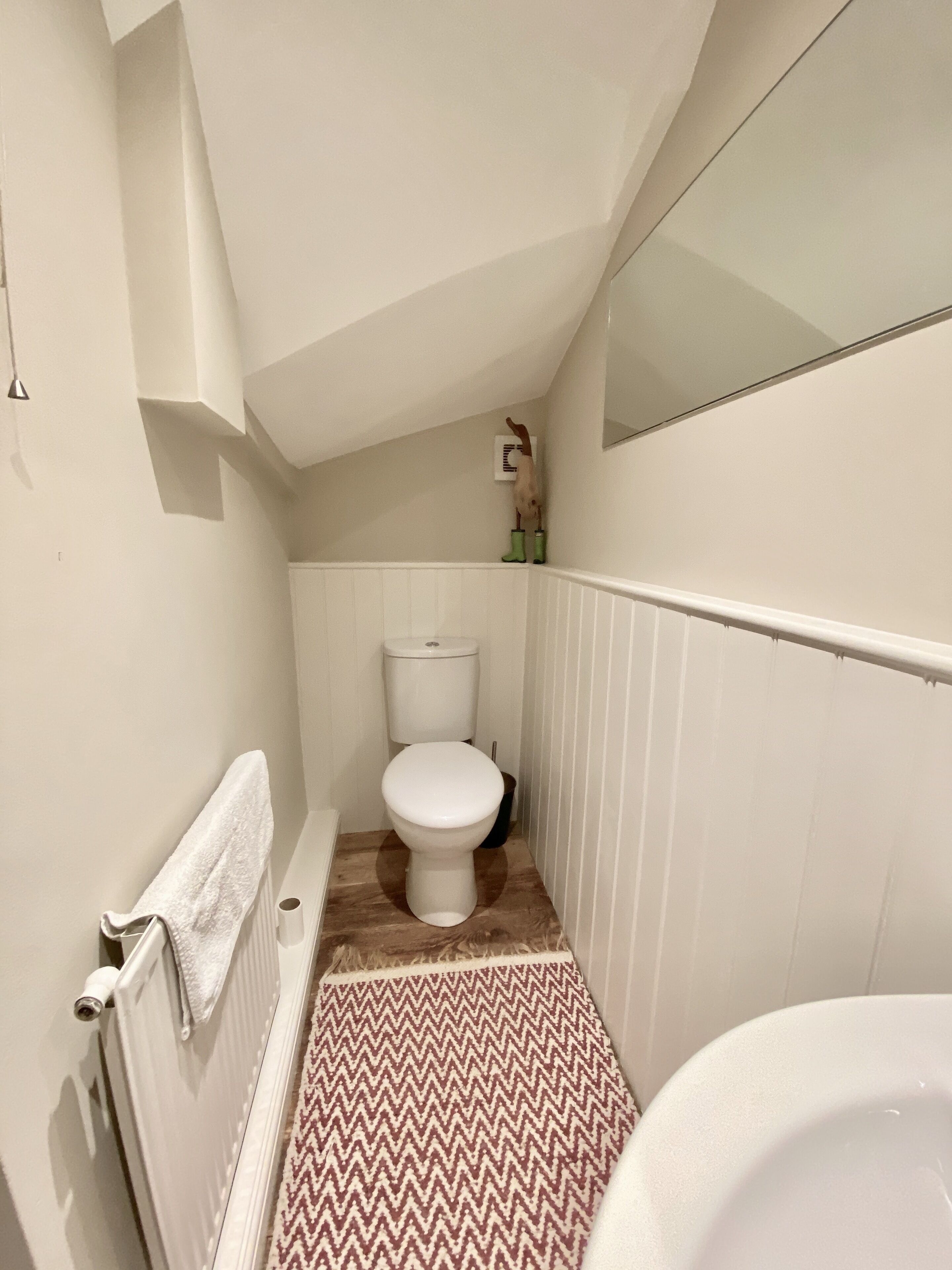 A narrow bathroom with a white toilet, a radiator, and a patterned floor.