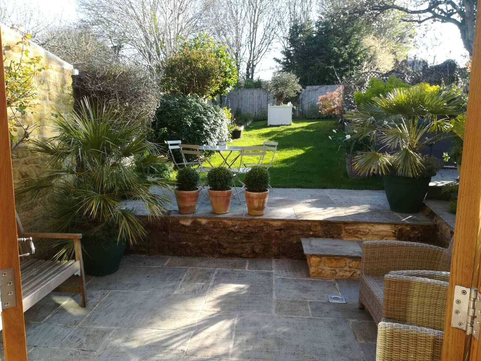 A patio with stone flooring, a wooden bench, and potted plants.