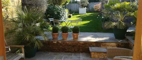 A patio with stone flooring, a wooden bench, and potted plants.