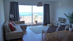 Een moderne woonkamer met een bank, fauteuils, een televisie en een balkon met uitzicht op zee.