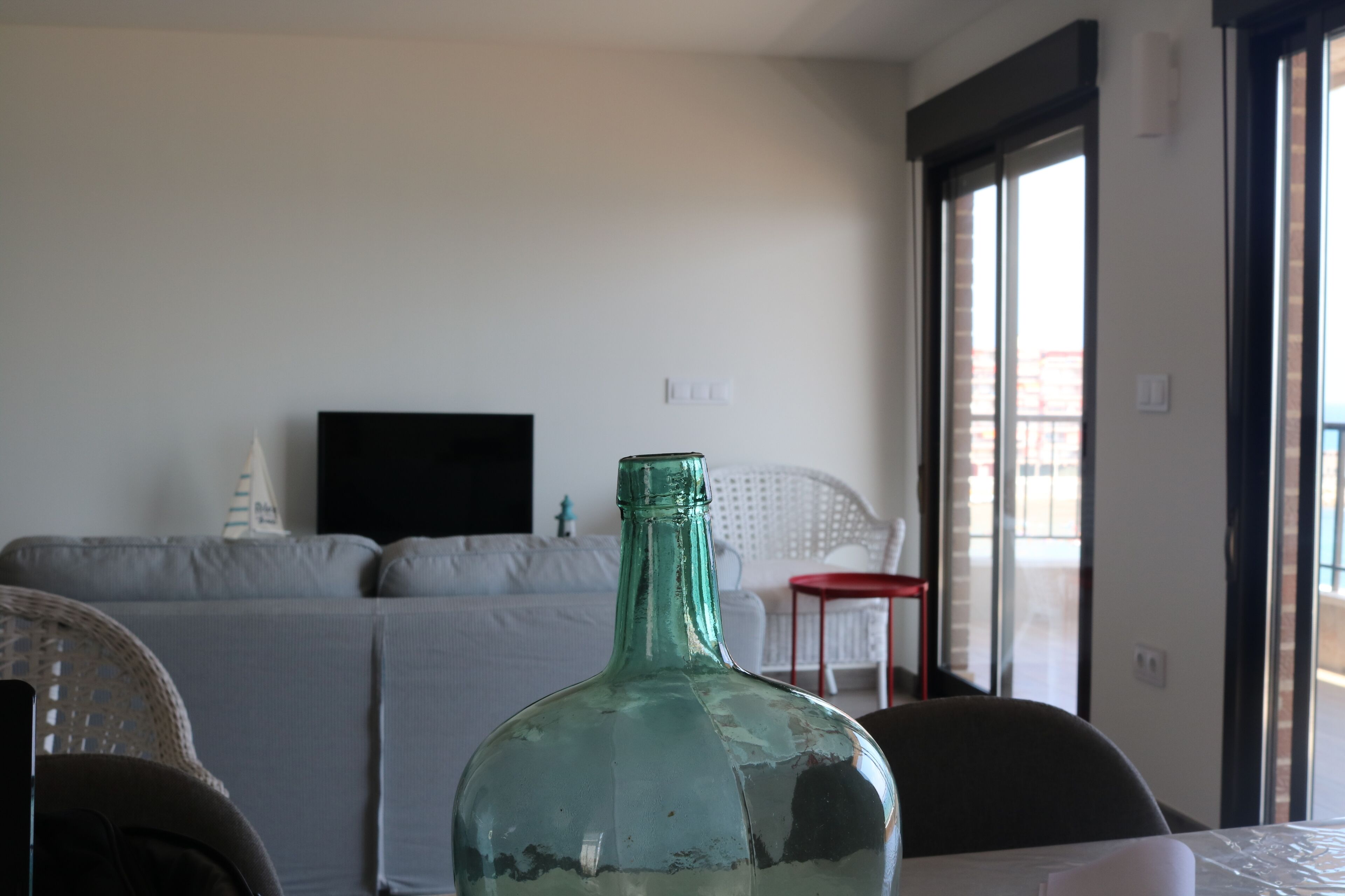 Una habitación con un ventanal amplio, un sofá, un televisor y una mesa con una botella.