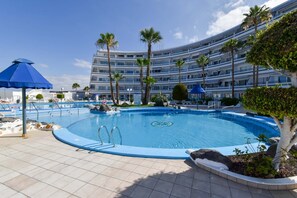 Una piscina con borde azul, palmeras y un edificio moderno al fondo.