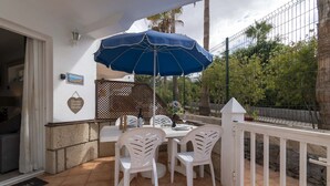 Een terras buiten met een tafel, stoelen, een blauwe parasol en een sierhekwerk.