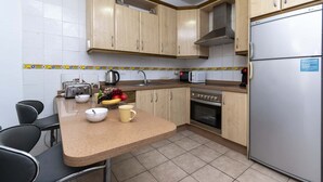 Een keuken met houten kastjes, een roestvrijstalen koelkast, een magnetron, een broodrooster en een spoelbak.
