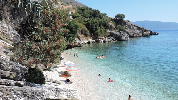 A beach with clear water, rocky cliffs, and people swimming and sunbathing. - Kalliroi - Exquisite Villa Designed Exclusively For Two with Large Private Pool. (Pylaros)