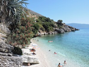 A beach with clear water, rocky cliffs, and people swimming and sunbathing.