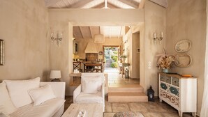 A spacious living room with a high ceiling, a sofa, a chair, a coffee table, and a cabinet with decorative items. - Kalliroi - Exquisite Villa Designed Exclusively For Two with Large Private Pool. (Pylaros)