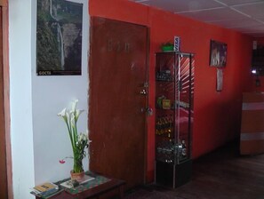 A room with a wooden door, a shelf with bottles, a small table with a plant, and a poster on the wall. - Hotel-Hostal Chachapoyas (Chachapoyas)