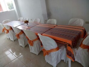 A conference room with a long table, white chairs with orange sashes, and a vase with flowers on the table. - Hotel-Hostal Chachapoyas (Chachapoyas)