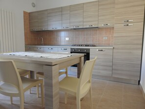 A modern kitchen with wooden cabinets, a gas stove, and a dining table with chairs. - Olive trees stay between sea and mountains (Altino)
