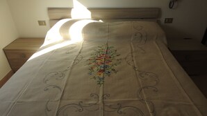 Una cama bien hecha con una colcha bordada de motivos florales, un cabecero de madera y una mesita de noche con una lámpara.