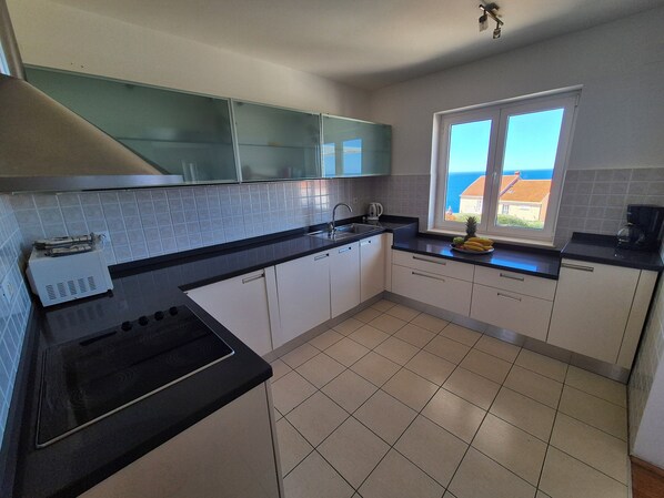 A kitchen with a stove, sink, and window with a view of the sea. - Villa Dubrovnik with pool and sea view (Dubrovnik)