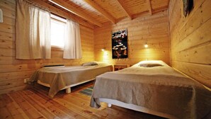 A cabin-style room with two single beds, wooden walls, and a window with curtains.
