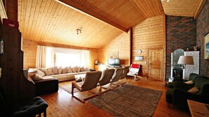 A cozy log cabin interior with a wooden ceiling, a fireplace, a sofa, and a television.