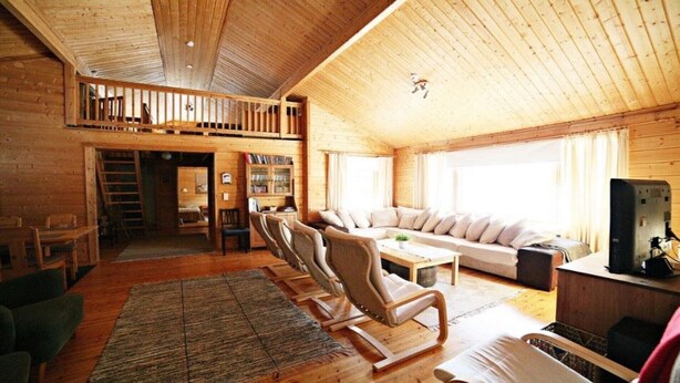 A cozy wooden cabin with a loft bedroom, a living room with a sofa and chairs, and a dining area.