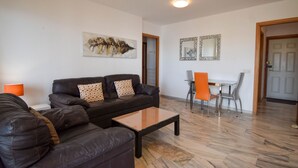 Een woonkamer met een donkerbruine leren bank, een bijzettafeltje en een oranje fauteuil. Aan de muur hangt een schilderij en erboven de fauteuil een spiegel.