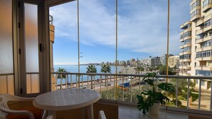 Een balkon met een tafel en stoelen, met uitzicht op een strand en stadsbeeld.