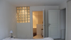 Un dormitorio con una cama, una mesita de noche, un ventanal con vidrio esmerilado y una puerta que da al baño.