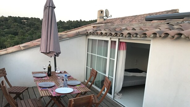 Una terraza en la azotea con una mesa lista para comer, sillas y una sombrilla grande.