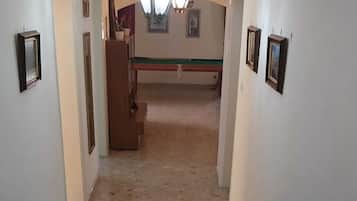 A hallway with a chandelier, framed pictures on the walls, and a bench.