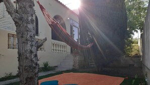 Un hamac est suspendu entre deux arbres dans une cour, où l’on trouve une pelouse verdoyante et un tapis rouge.