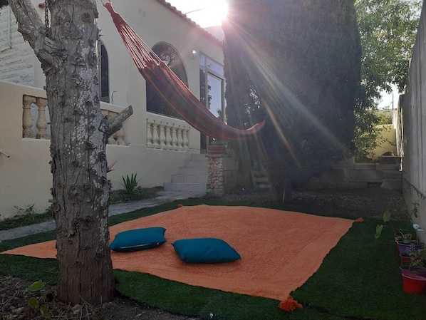 A hammock tied between trees in a courtyard with a green lawn and a red mat.