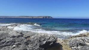 Une côte rocheuse bordée d’eaux d’un bleu limpide et dominée par une falaise lointaine.