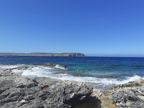 Une côte rocheuse bordée d’eaux d’un bleu limpide et dominée par une falaise lointaine.