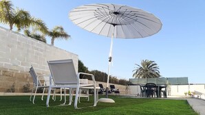 Une terrasse avec un parasol blanc, des chaises en métal blanc et une table.