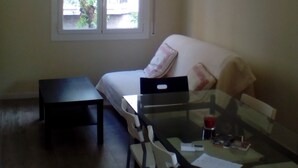 A small, well-lit room with a bed, a table, and a chair. There is a window providing natural light and a view of the outside. - Castel apartment Fira (L'Hospitalet de Llobregat)