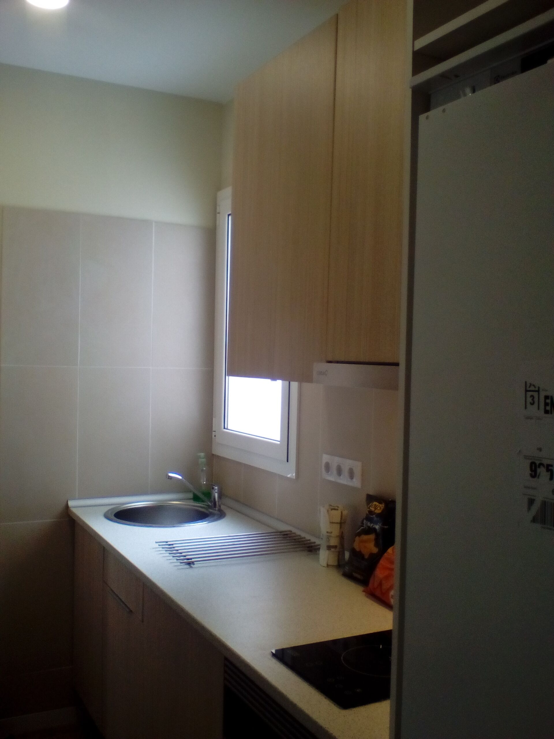 Eine kleine Küche mit Spüle, Fenster und Kühlschrank.