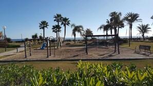Un parco con giochi per bambini, panchine e palme.