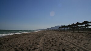 Una spiaggia con impronte che conducono a una fila di ombrelloni di paglia.