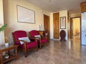 A spacious room with a wooden floor, two red armchairs, a small table with a plant, and a large abstract painting on the wall.