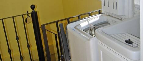 A laundry area with a washing machine and dryer, a window with a view of a hilly landscape, and a black metal railing.