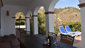 Une terrasse couverte avec une table, des chaises et une bouteille de vin.