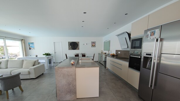 Una cocina moderna con una isla central, electrodomésticos de acero inoxidable y una zona de comedor con sofá y mesa.