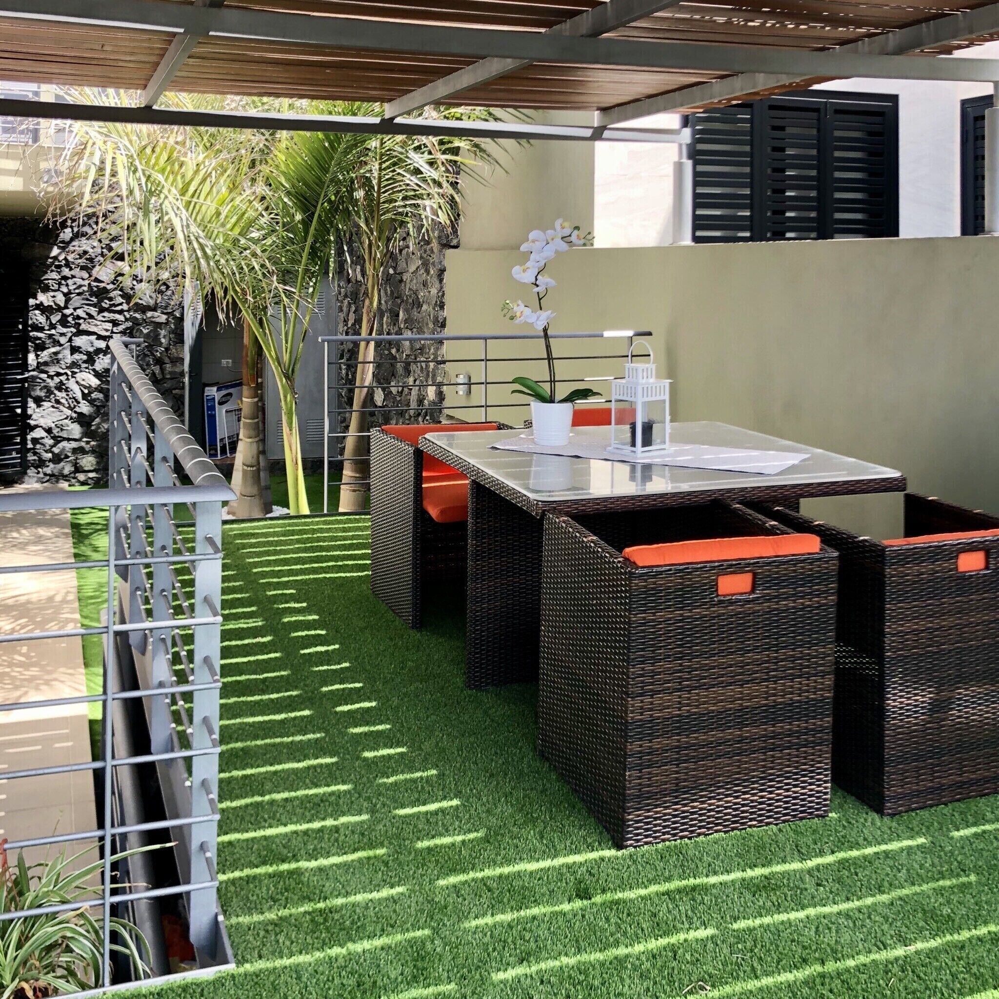 An outdoor patio with a glass table, wicker furniture, and artificial grass.