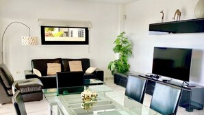 Una sala de estar moderna con una mesa de comedor de vidrio, un sofá de cuero negro y un televisor de pantalla plana grande montado en la pared.