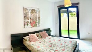 Un dormitorio con cama, un cuadro y una puerta corrediza de vidrio al exterior.