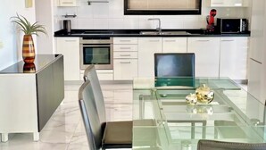 Una cocina moderna con armarios blancos, una mesa de comedor de vidrio y un horno empotrado.