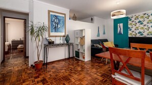 Un salon moderne avec un parquet en bois, un coin repas comprenant une table et des chaises en bois, un canapé et une bibliothèque.
