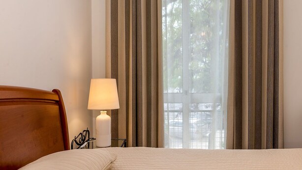 Une chambre d’hôtel avec un lit, une table de chevet avec une lampe et une fenêtre avec des rideaux à rayures.