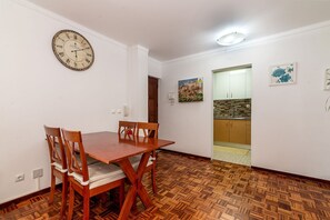 Een eetgedeelte met een houten tafel en stoelen, een wandklok en een keuken die zichtbaar is door een open deur.