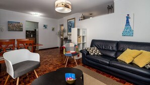 Un salon comprenant un canapé en cuir noir, une table à manger en bois avec des chaises, une table basse noire avec un bol décoratif, un fauteuil blanc et un luminaire suspendu.