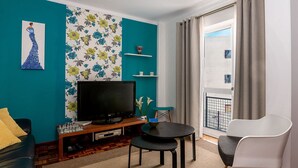 Un salon aux murs de couleur turquoise, doté d’un téléviseur à écran plat, d’un jeu d’échecs et d’un coin repas avec une chaise blanche et une petite table.