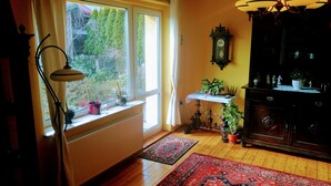 A room with a large window, radiator, wooden floor, and a dark wooden cabinet with decorative items.
