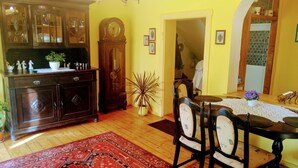 A traditional dining area with a wooden table and chairs, a red patterned rug, a cabinet with glass doors, and a large potted plant.