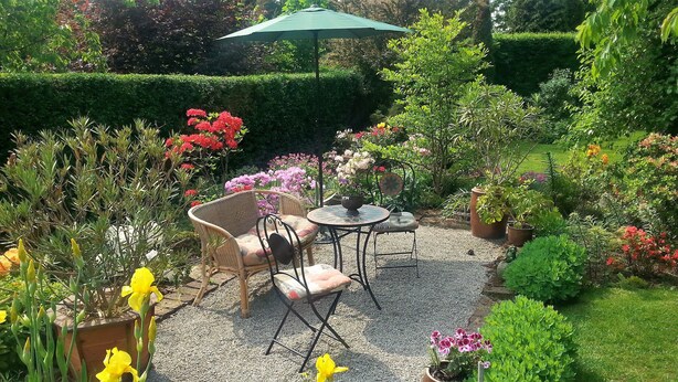 A garden patio with wicker furniture, a round table, and a green umbrella.