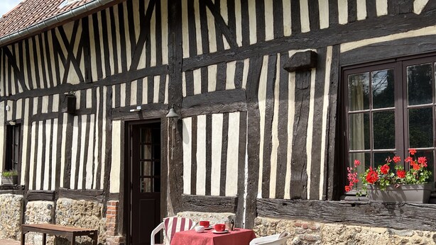 A half-timbered building with a stone wall, a wooden bench, a table with a red tablecloth, and a window with red flowers. - A pastoral setting within reach of seaside (12-25 kms) - Sleeps 6-8 (Manneville-La-Raoult)